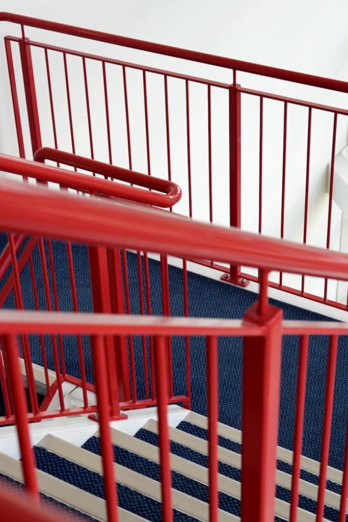 A modern indoor staircase with vibrant red railings and blue carpeted steps.